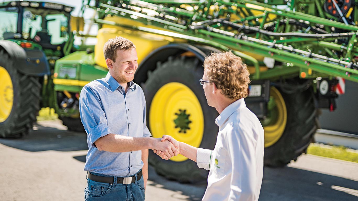 Edasimüüja ja kliendi käepigistus John Deere’i pritsi ees.