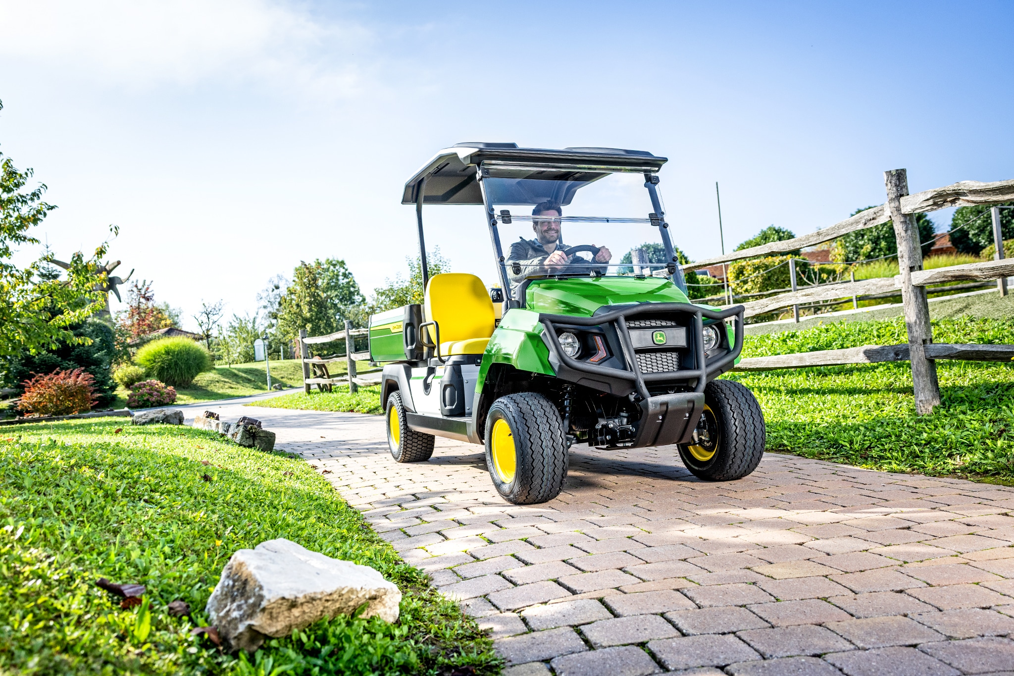 Töö- ja vabaajasõiduk Gator GS sõidab kujundatud maastikuga ala sillutatud teel Töö- ja vabaajasõiduk Gator GS sõidab kujundatud maastikuga ala sillutatud teel