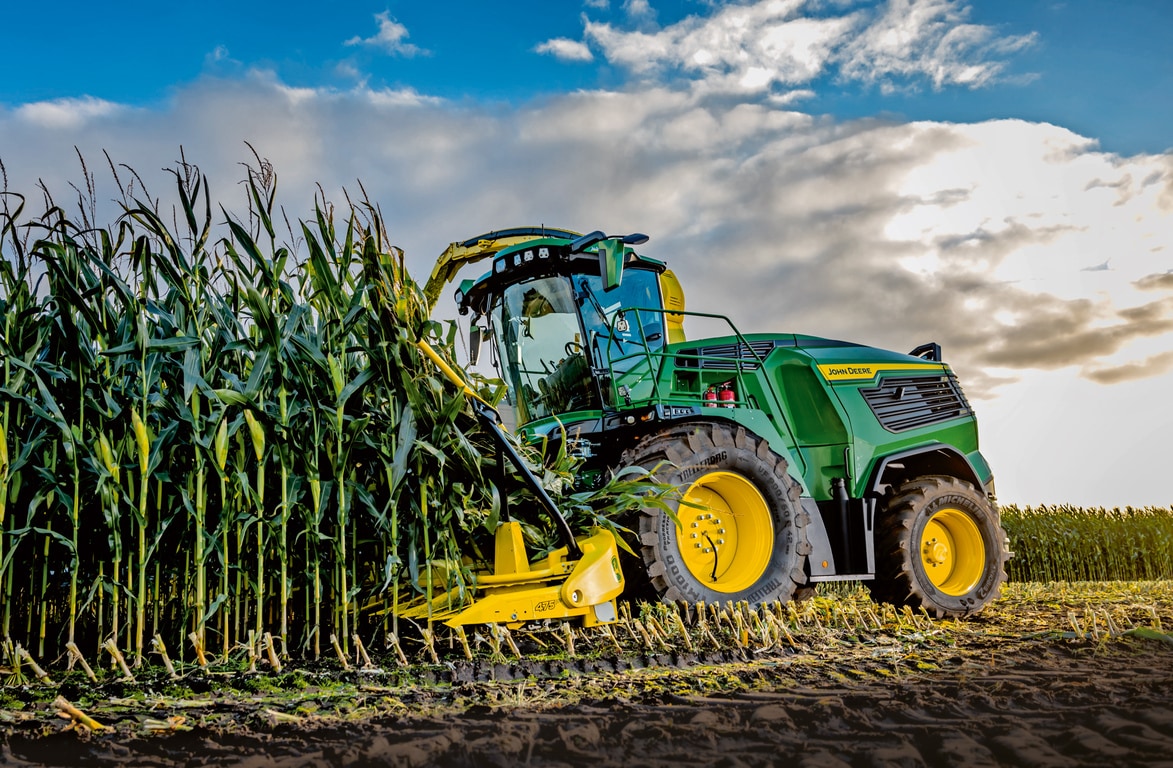 John Deere'i hekseldi koristab maisi põllul sinise pilvise taeva all.