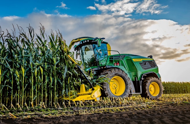 John Deere'i hekseldi koristab maisi põllul sinise pilvise taeva all.