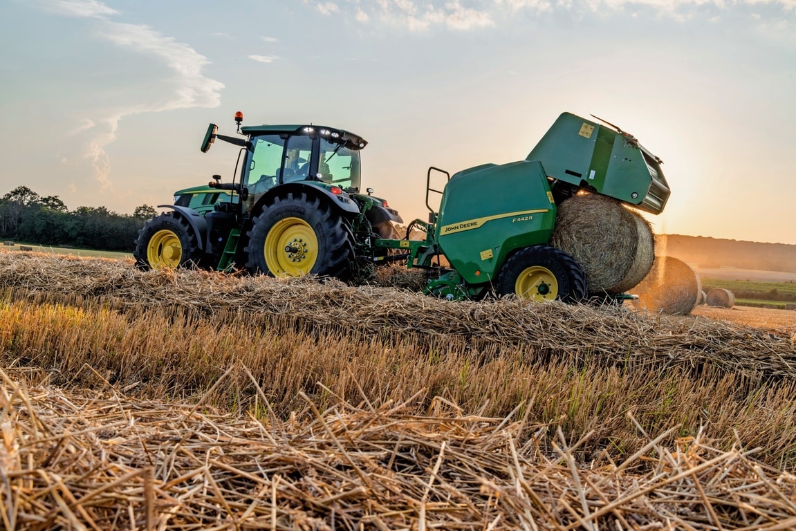 John Deere'i F442M rullipress, mida tõmbab John Deere'i 6M traktor, mis väljutab põhupalli