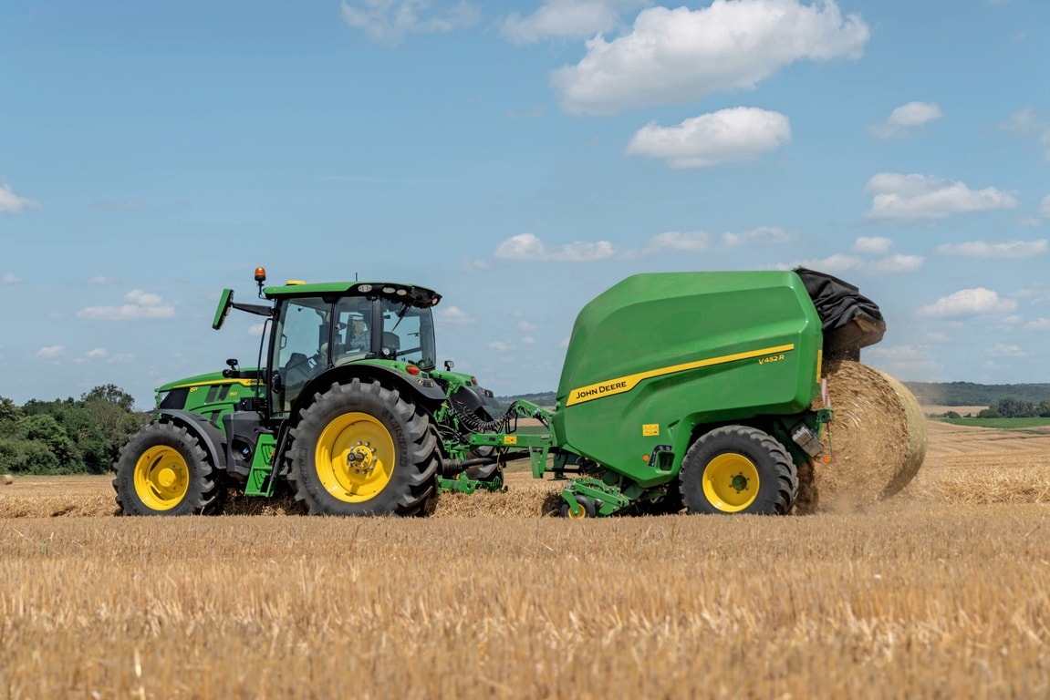 John Deere V452R põhuväljal, mida tõmbab John Deere'i 6R 150 rulli väljastav masin