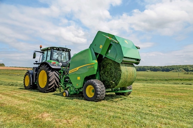 John Deere'i F442M rullipress, mida veab John Deere'i 6M traktor, väljastades heinapalli