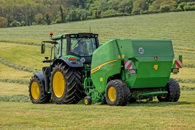 John Deere'i F442M rullipress, mida veab künklikul muruväljakul John Deere'i 6M traktor